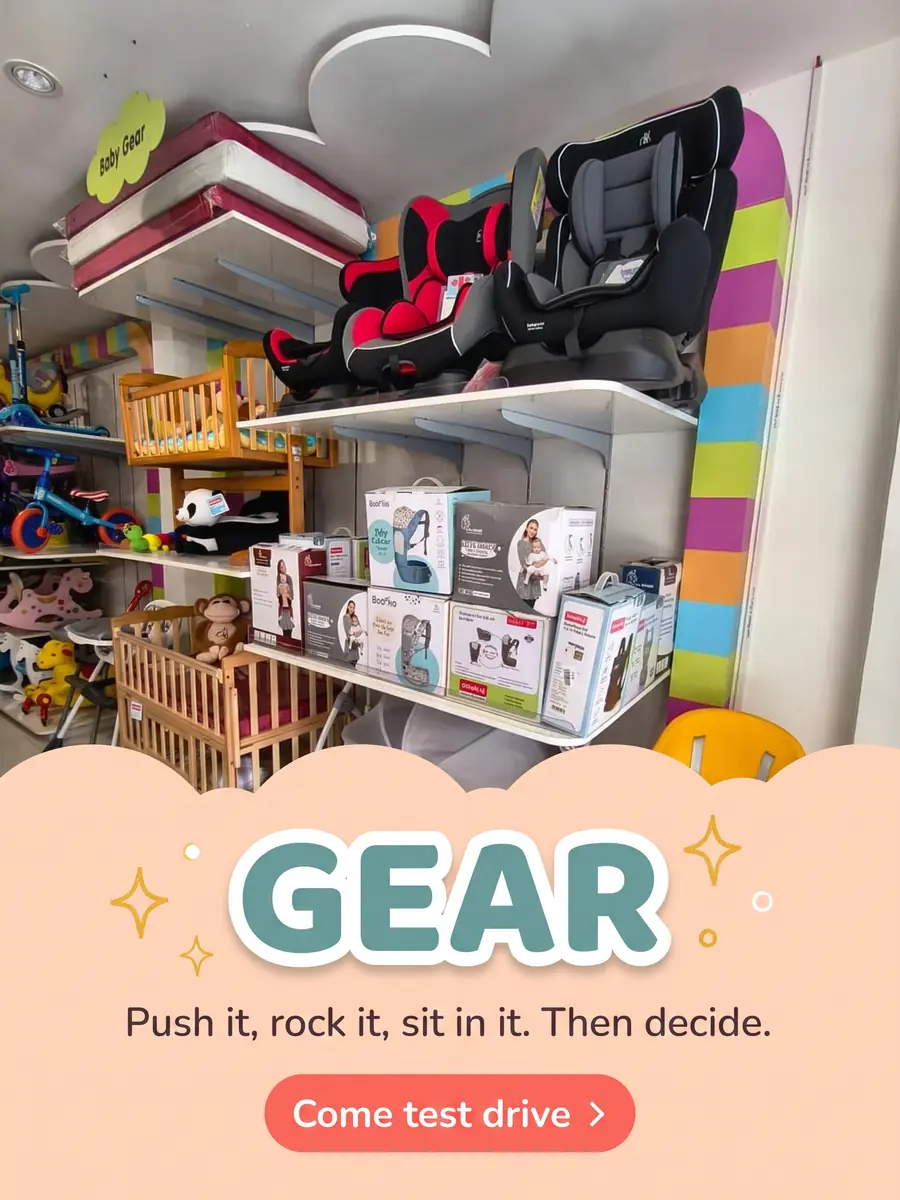 The baby gear aisle — car seats, wooden cots, a high chair and boxed carriers. Text on the photo: Gear — push it, rock it, sit in it, then decide. Come test drive.